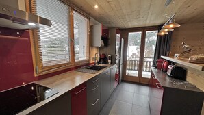 Een moderne keuken met een houten plafond, een groot raam met zonwering, een ingebouwde kookplaat en een koelkast.