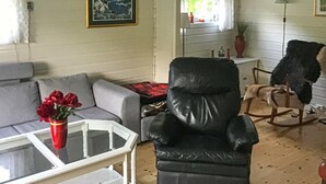 A living room with a grey sofa, a black leather chair, a rocking chair, a glass coffee table with a red vase, and a framed picture on the wall. - 2 bedroom stunning home in Flekkefjord (Flekkefjord)