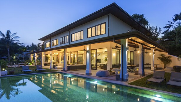 Uma casa moderna de dois andares com piscina, área de estar externa e grandes janelas.