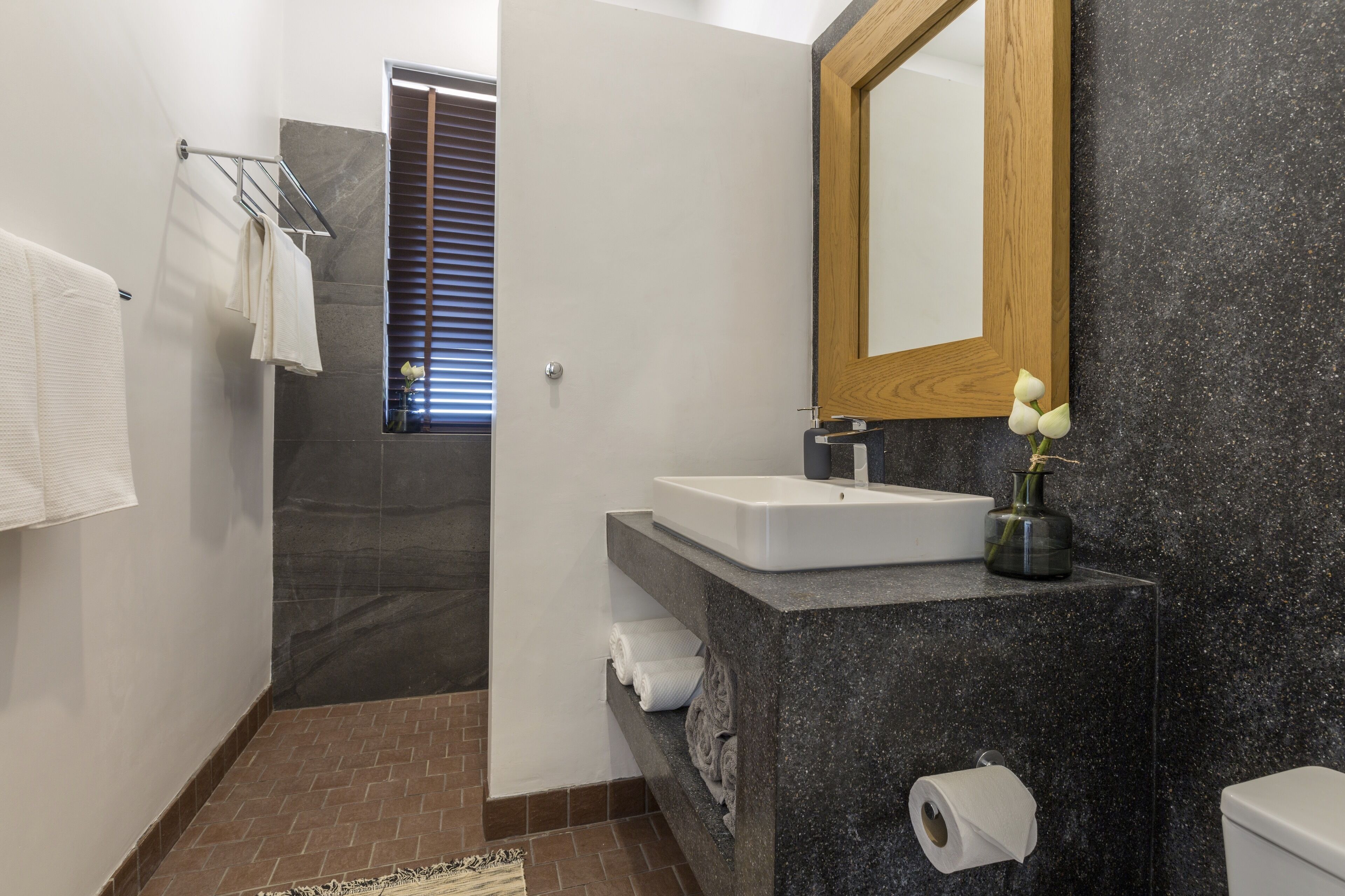 A modern bathroom with a marble sink, a wooden-framed mirror, and a shower area.