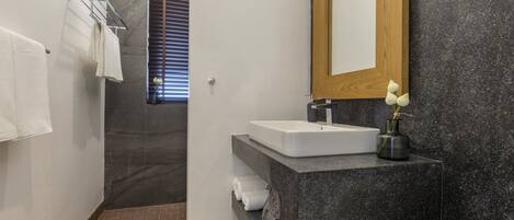 A modern bathroom with a marble sink, a wooden-framed mirror, and a shower area.