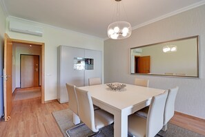 A dining area with a white table, four chairs, a chandelier, and a large mirror on the wall.