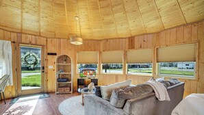Habitació acollidora amb sostre de fusta, un sofà gris, televisió i vista cap a l'exterior.