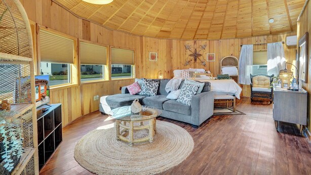 Interior acollidor d'una cabana amb sostre de fusta, un sofà, un llit i una taula de menjador.