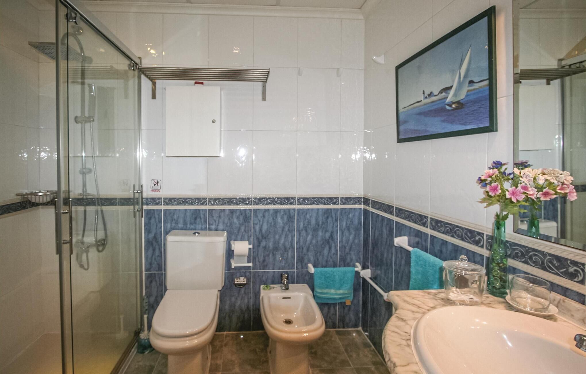 Ein Badezimmer mit Duschkabine, Toilette, Bidet, Waschbecken und einem Spiegel mit einem Gemälde.