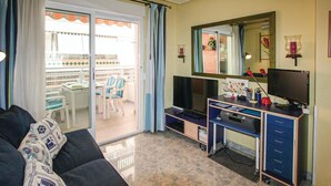 Een woonkamer met een bank, een televisie, een bureau met een computer, en een balkon met stoelen en een tafel.
