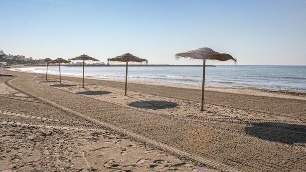 Een strand met rijen strooien parasols en een helder uitzicht op zee.