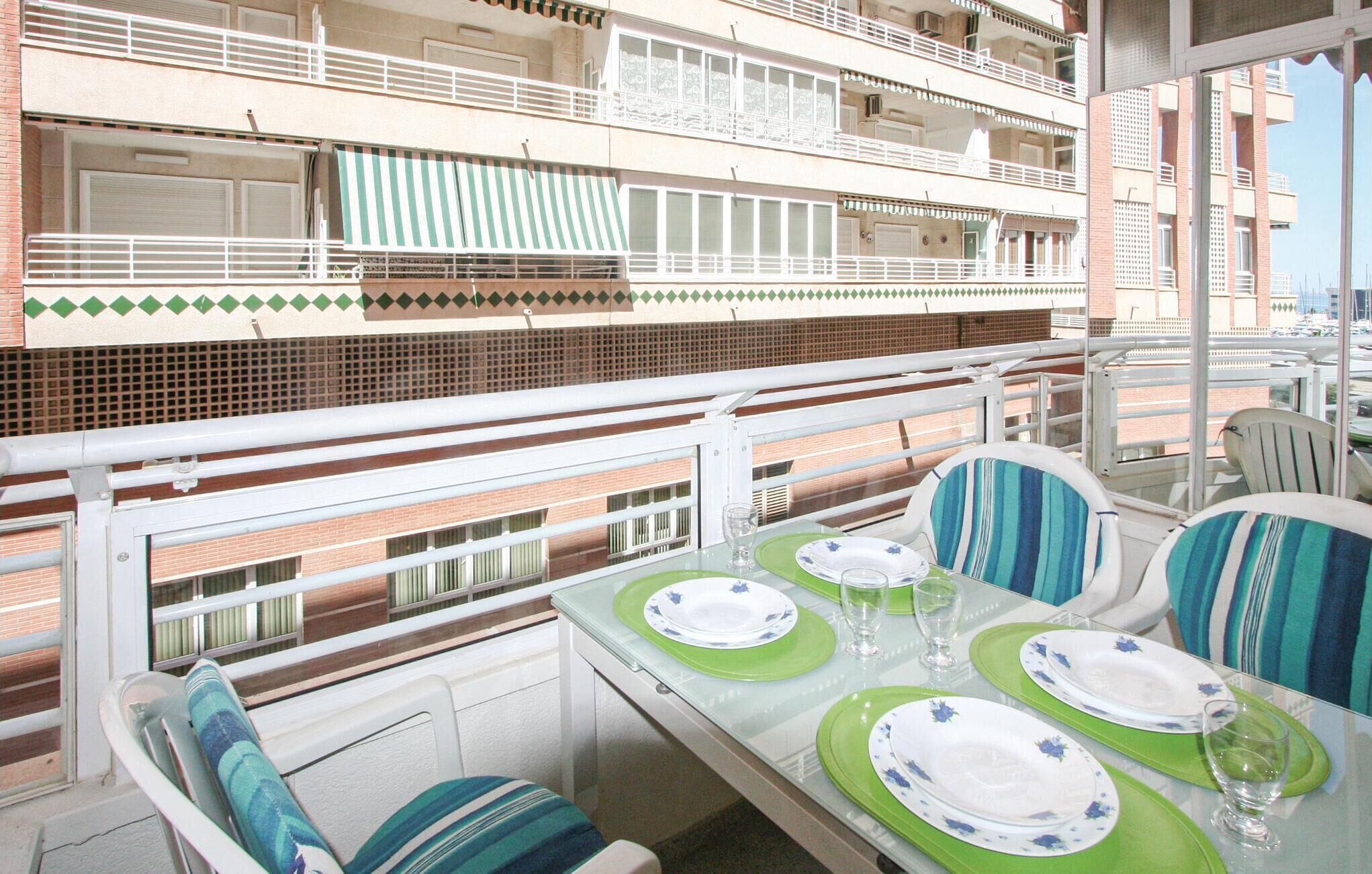 A balcony with a table set for dining, featuring green and white plates, and striped chairs.