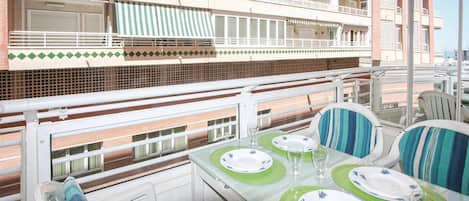 A balcony with a table set for dining, featuring green and white plates, and striped chairs.