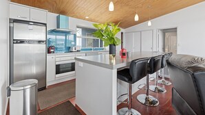 A modern kitchen with a stainless steel refrigerator, a coffee machine, and a large island with bar stools.