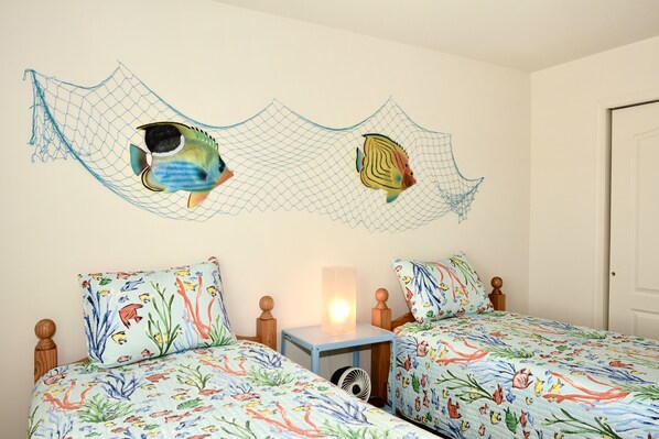 Een slaapkamer met twee bedden, een nachtkastje, een wandlamp en een decoratief net met vissen.
