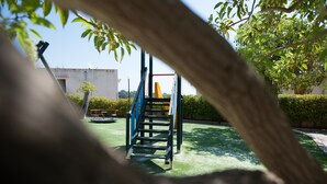 A playground with a blue climbing structure and a yellow slide, surrounded by greenery and a building in the background. - Apartment 250 meters from the beach with sea view (Provincia di Agrigento)