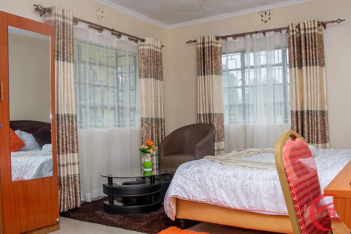 A bedroom with a bed, a chair, a small table, and a mirror.