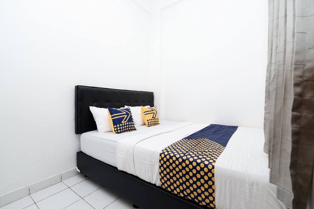 Una cama con cabecera negra, ropa de cama blanca y mantas estampadas.