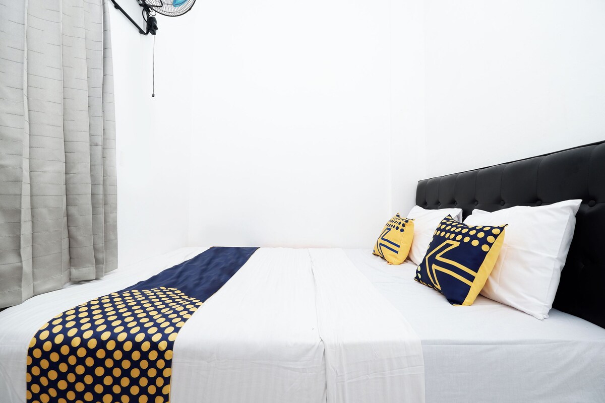 A neatly made bed with white bedding and a blue and yellow polka dot blanket.