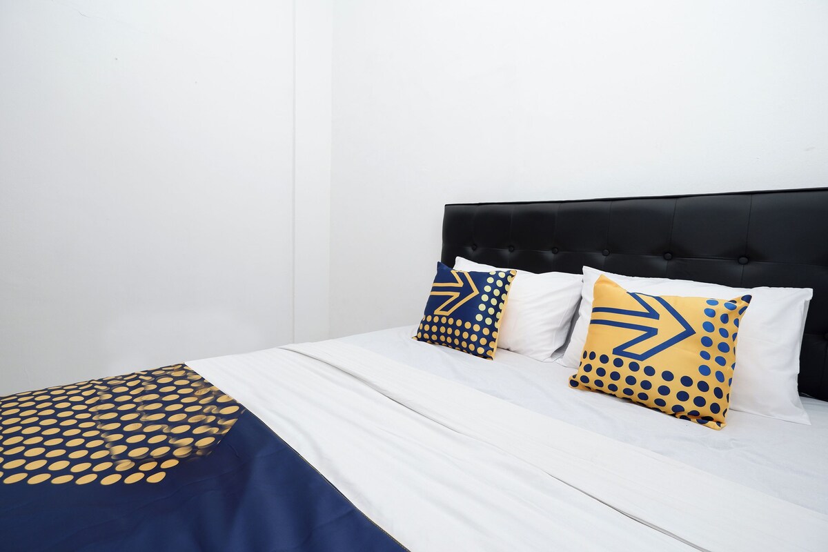 A bed with a white and blue bedspread, two pillows with geometric patterns, and a black upholstered headboard.