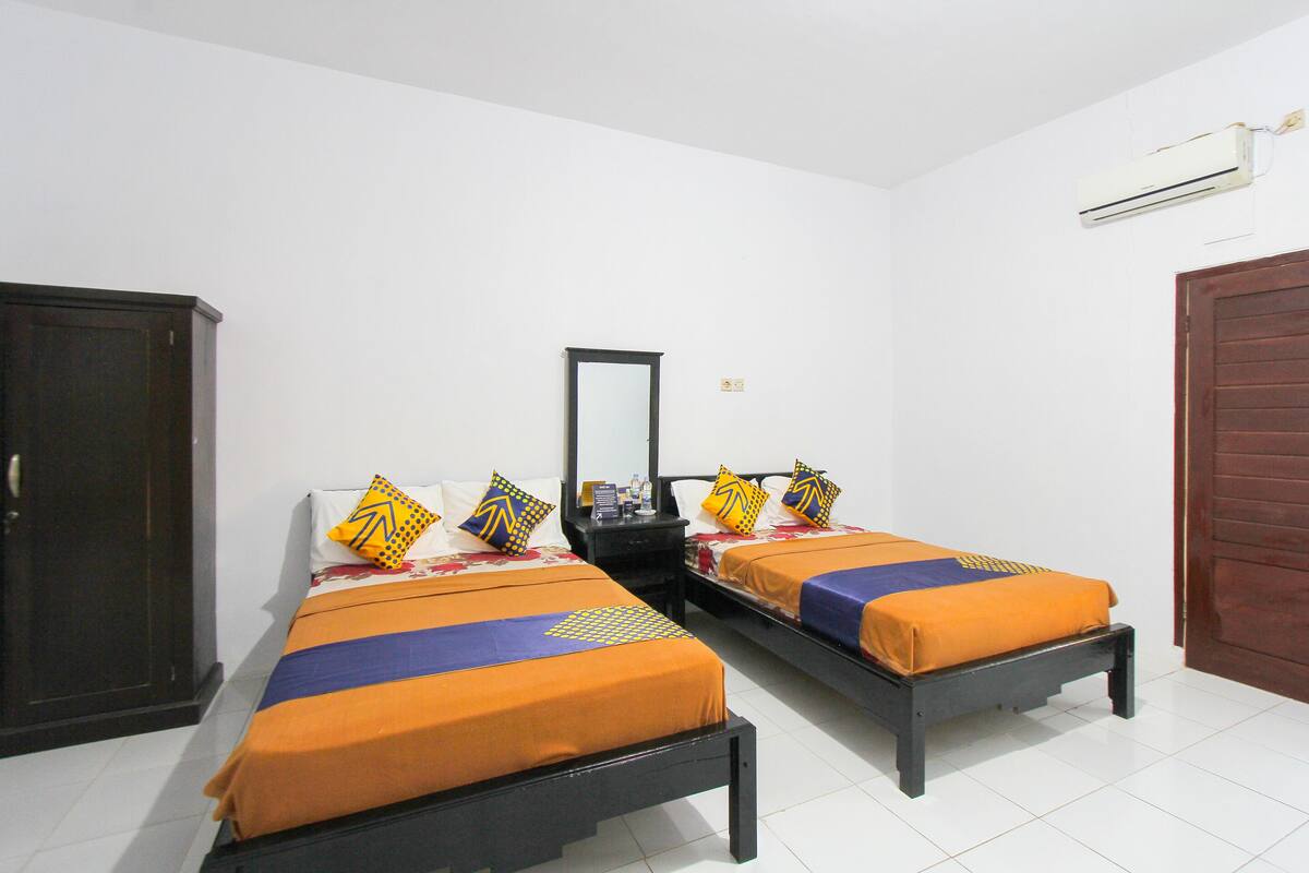 A room with two single beds, a wardrobe, a mirror, and an air conditioning unit.