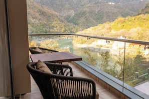Un balcón con vistas a un río y montañas. Hay dos sillas y una mesa.