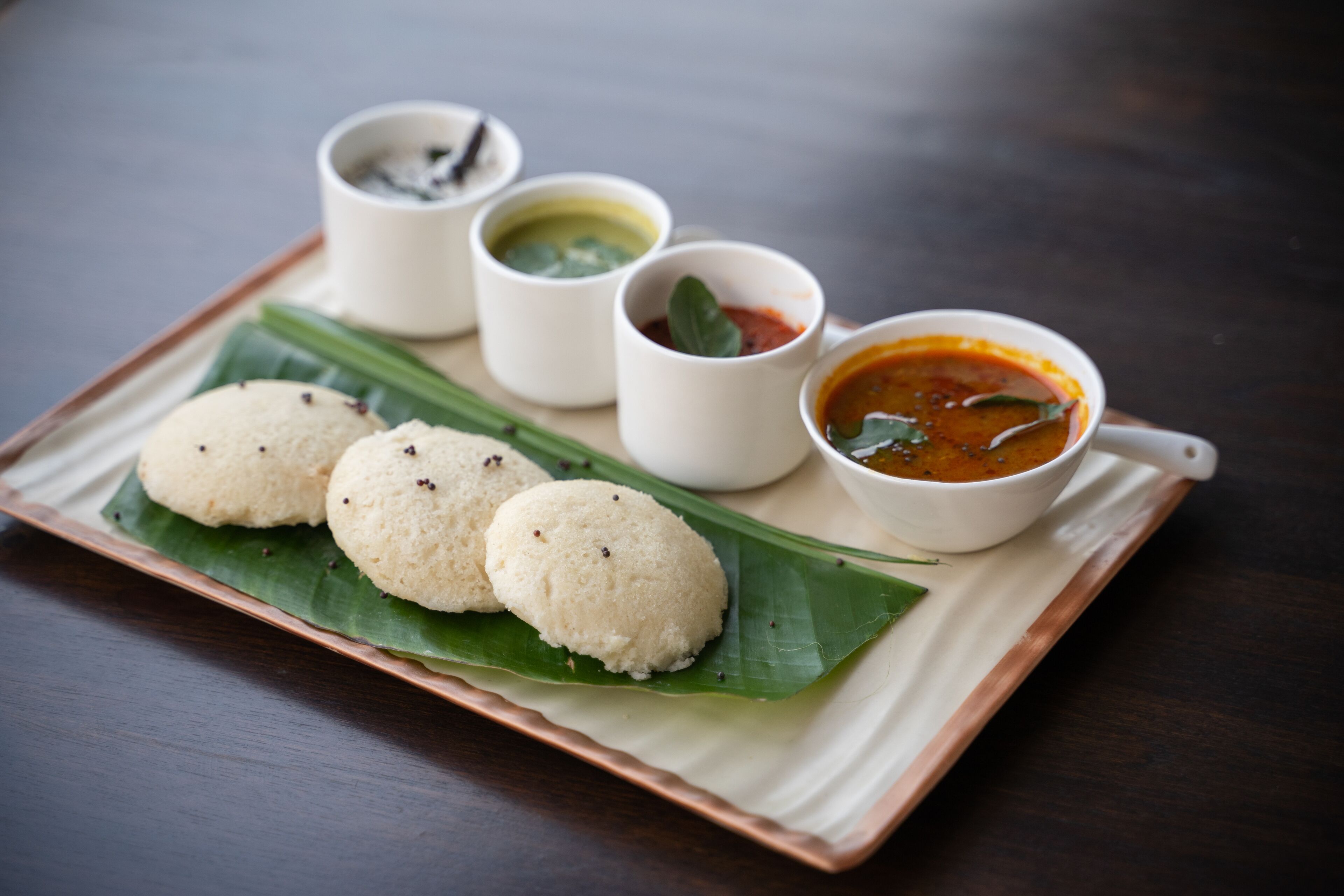 A plate of idlis with three different chutneys and a bowl of sambar.