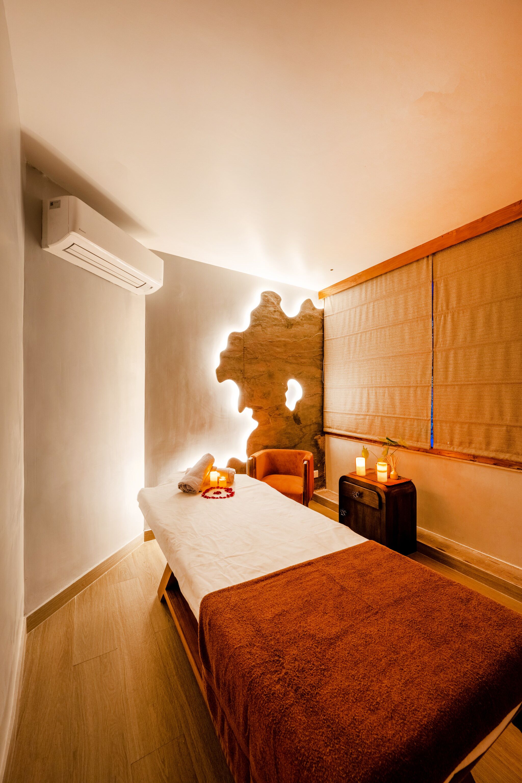 A spa room with a massage table, a wooden headboard, a small bedside table with candles, and a wall-mounted air conditioner.