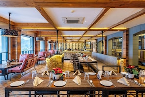 Un restaurante con vigas de madera, amplias ventanas y una larga mesa de comedor lista para una comida.