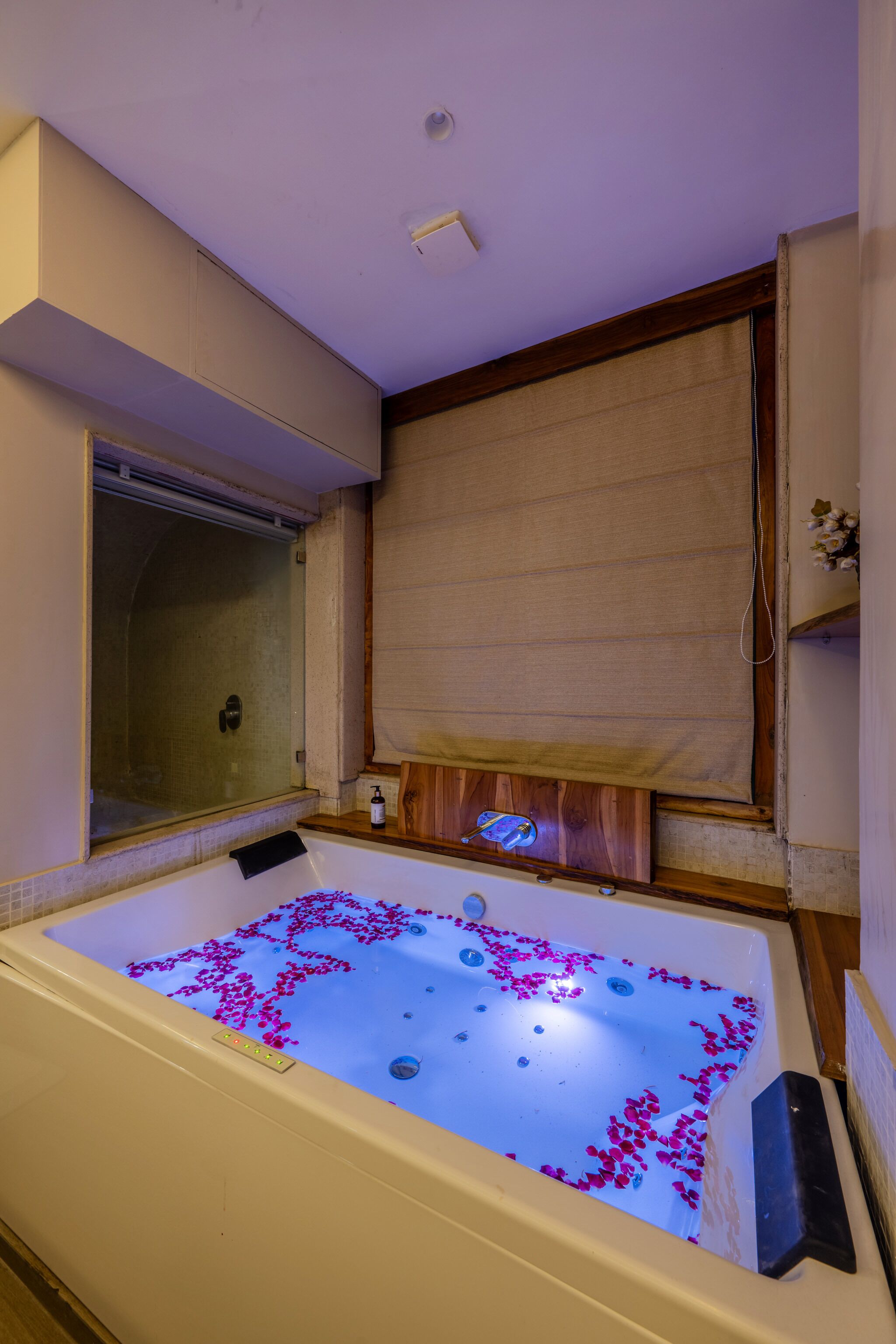 A bathroom with a bathtub filled with water and rose petals, a shower, and a wooden panel above the bathtub.