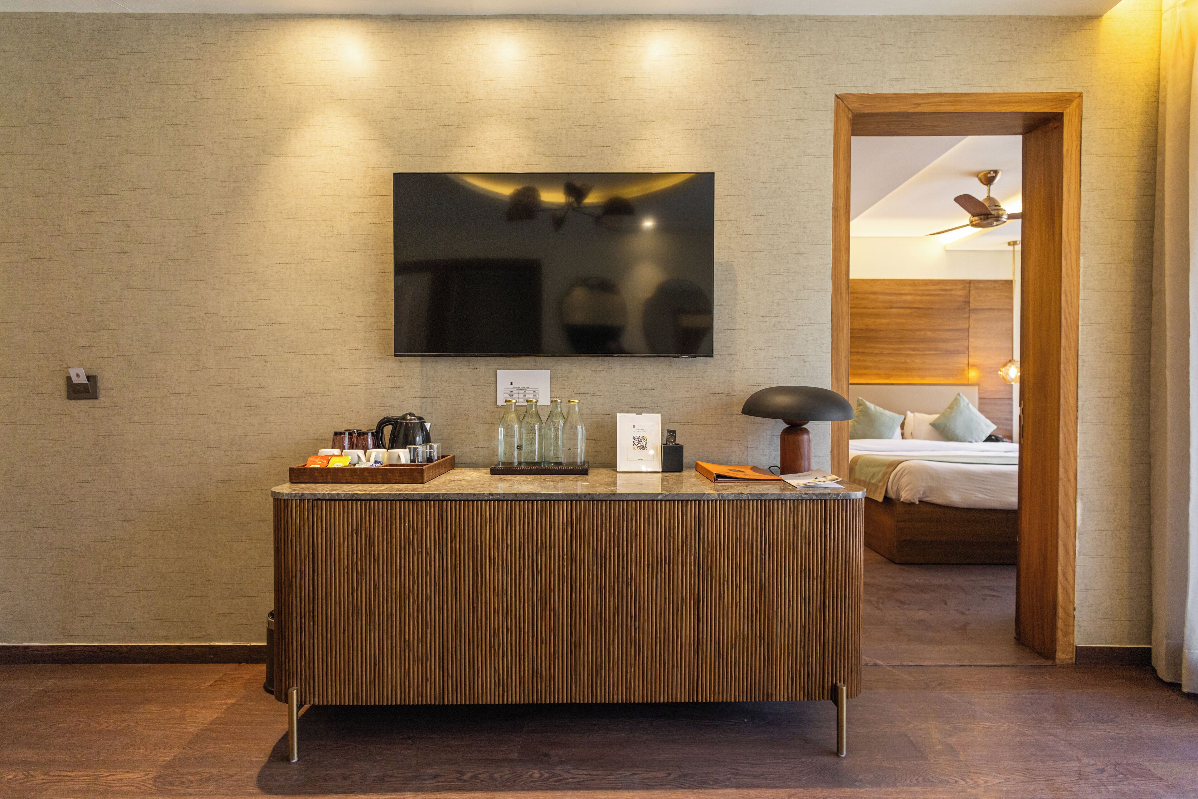 Una habitación de hotel moderna con un mostrador de recepción de madera, un televisor de pantalla plana montado en la pared y una cama con cabecero de madera.