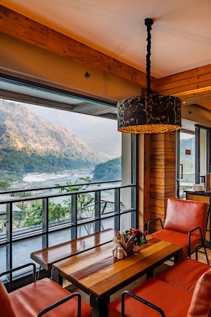 Comedor con mesa de madera y sillas rojas, con vistas a un paisaje montañoso a través de amplios ventanales.