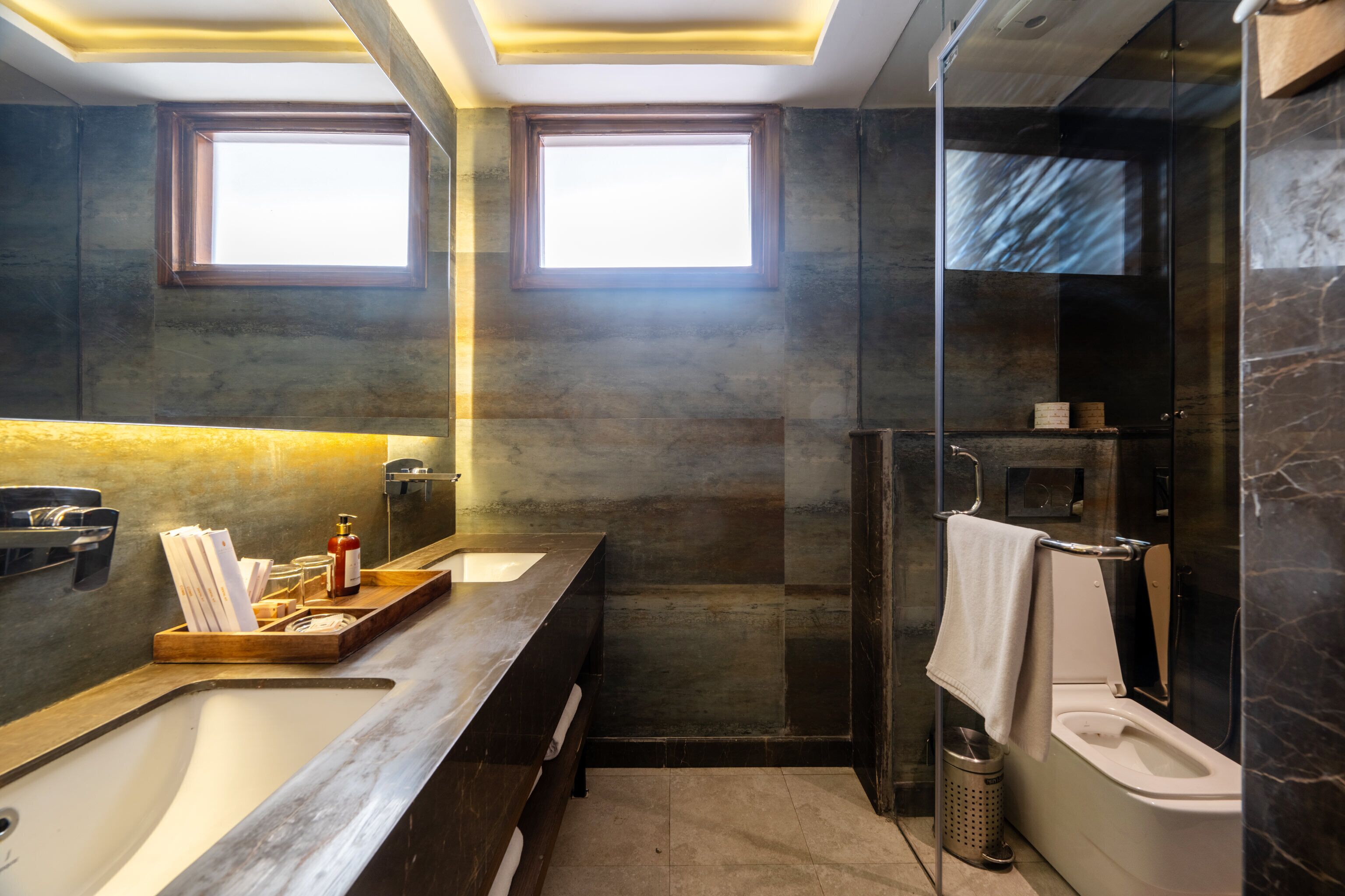 A modern bathroom with a large bathtub, a separate shower area, and two windows providing natural light.