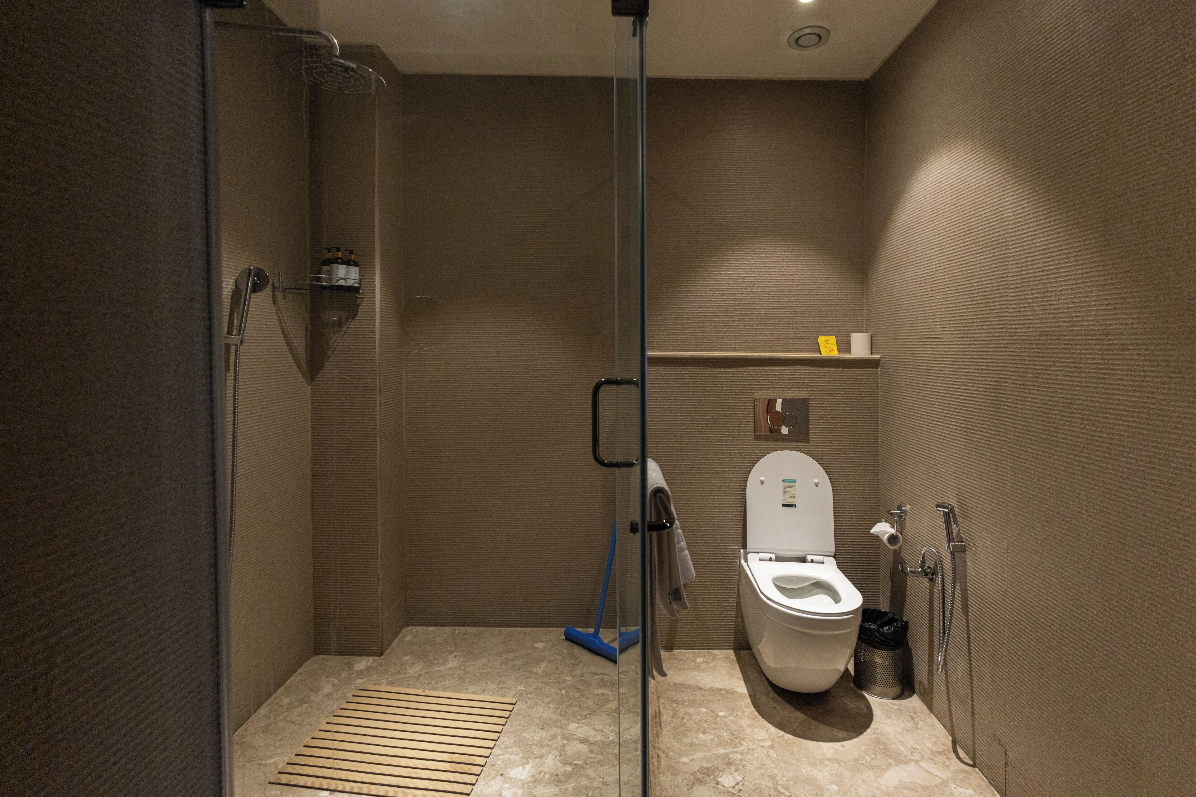 Uma casa de banho moderna com chuveiro em cabine de vidro, sanita e uma pequena prateleira com artigos de higiene pessoal.