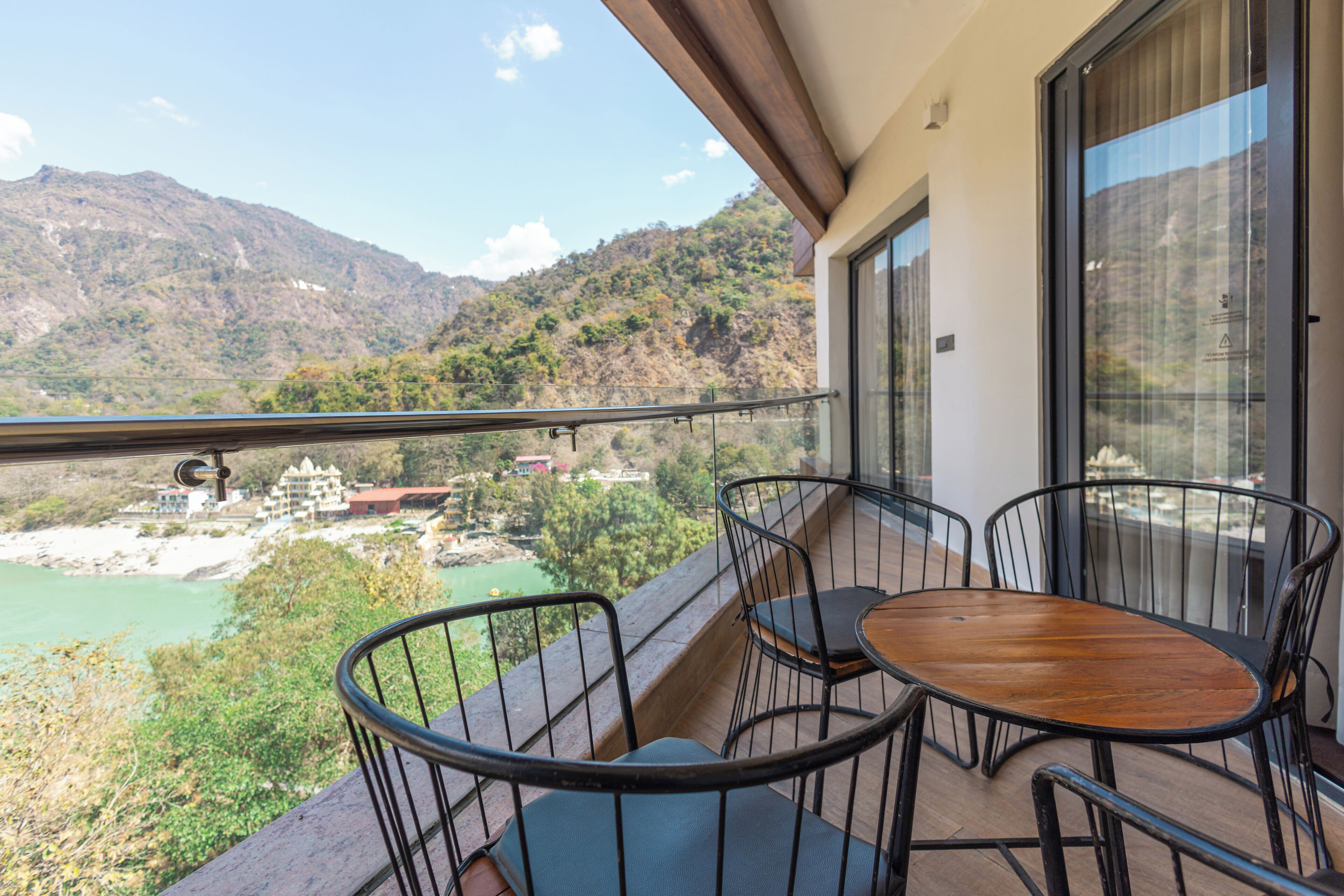 Ein Balkon mit Holztisch und -stühlen, mit Blick auf einen Fluss und Berge.