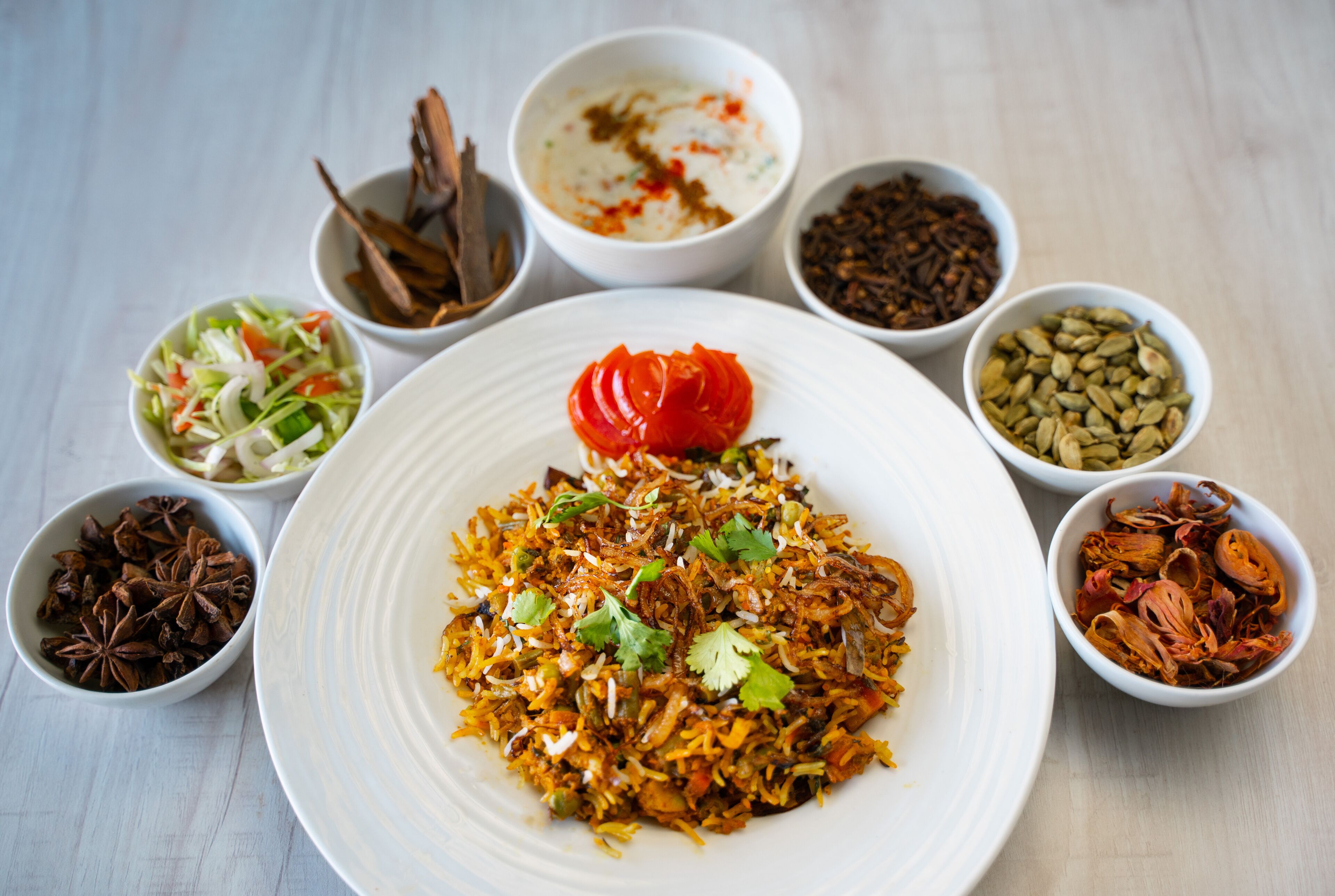 A plate of biryani with various side dishes including a salad, spices, and a dollop of sauce.