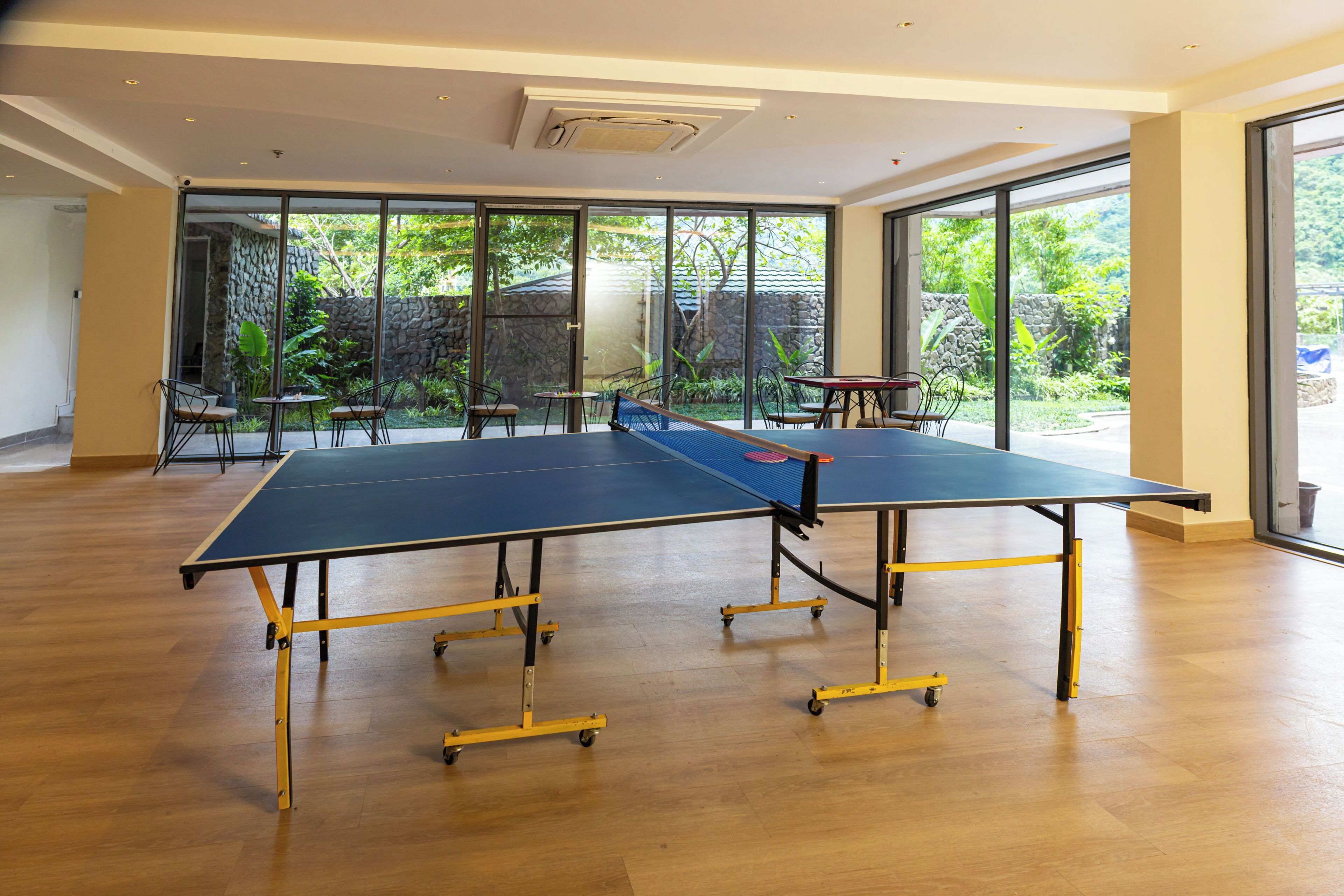 Amplio espacio interior con mesa de ping pong, sillas y ventanas grandes con vistas a zonas verdes.