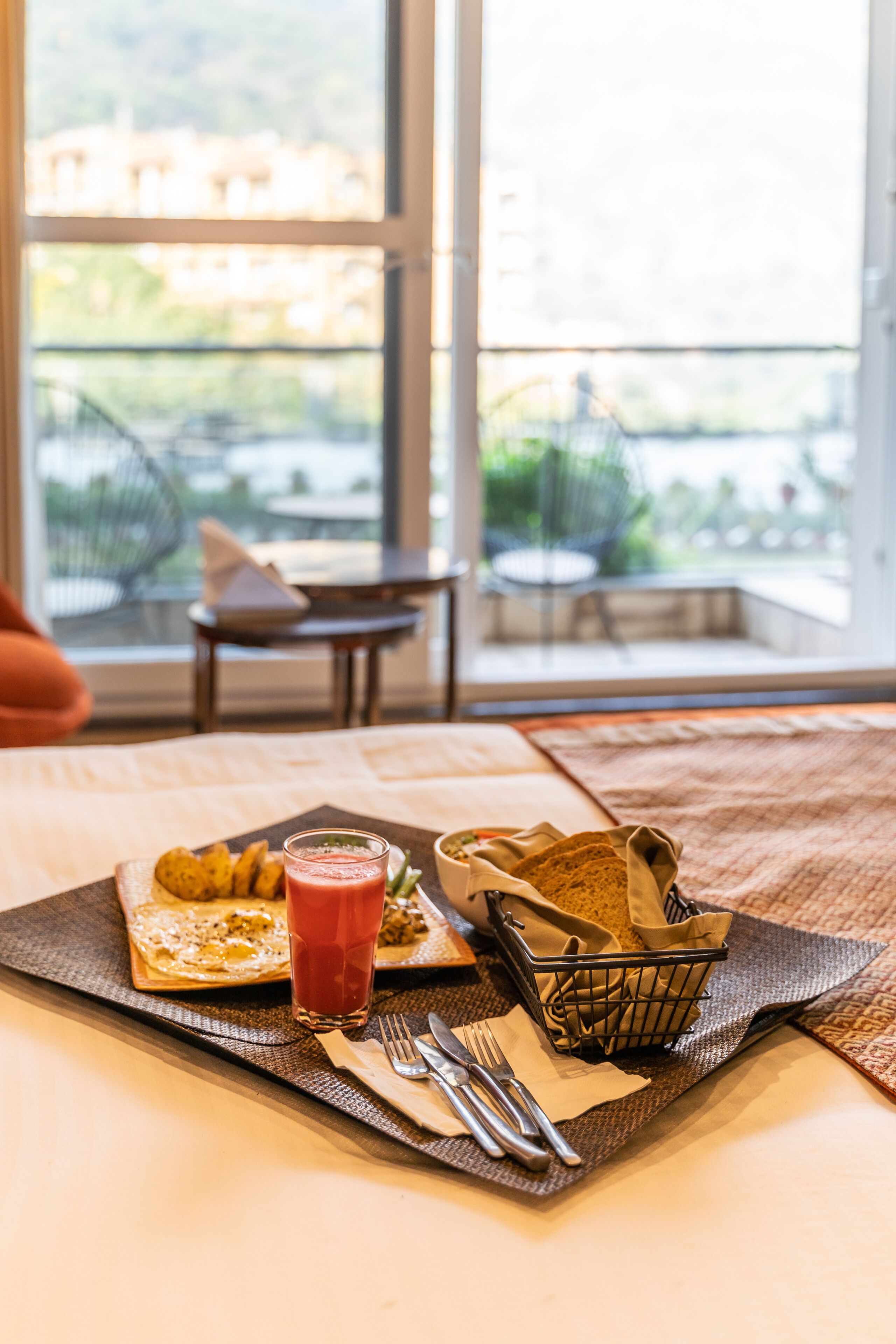 Une table mise pour le petit-déjeuner, avec une assiette de nourriture, un verre de jus rouge et un panier de pain.