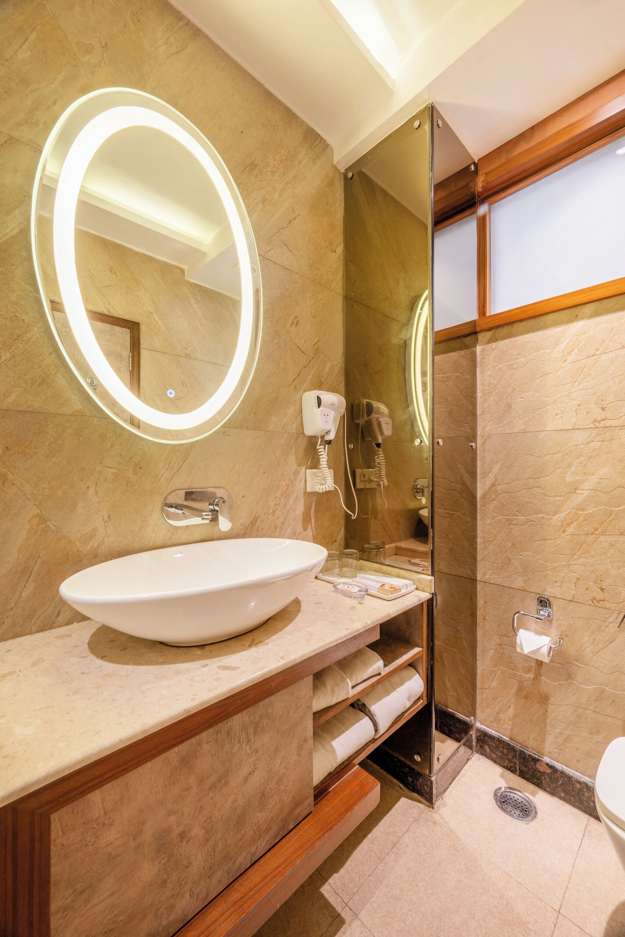 Une salle de bain moderne avec un grand lavabo ovale, un miroir rond avec éclairage intégré, une douche en verre et des toilettes.