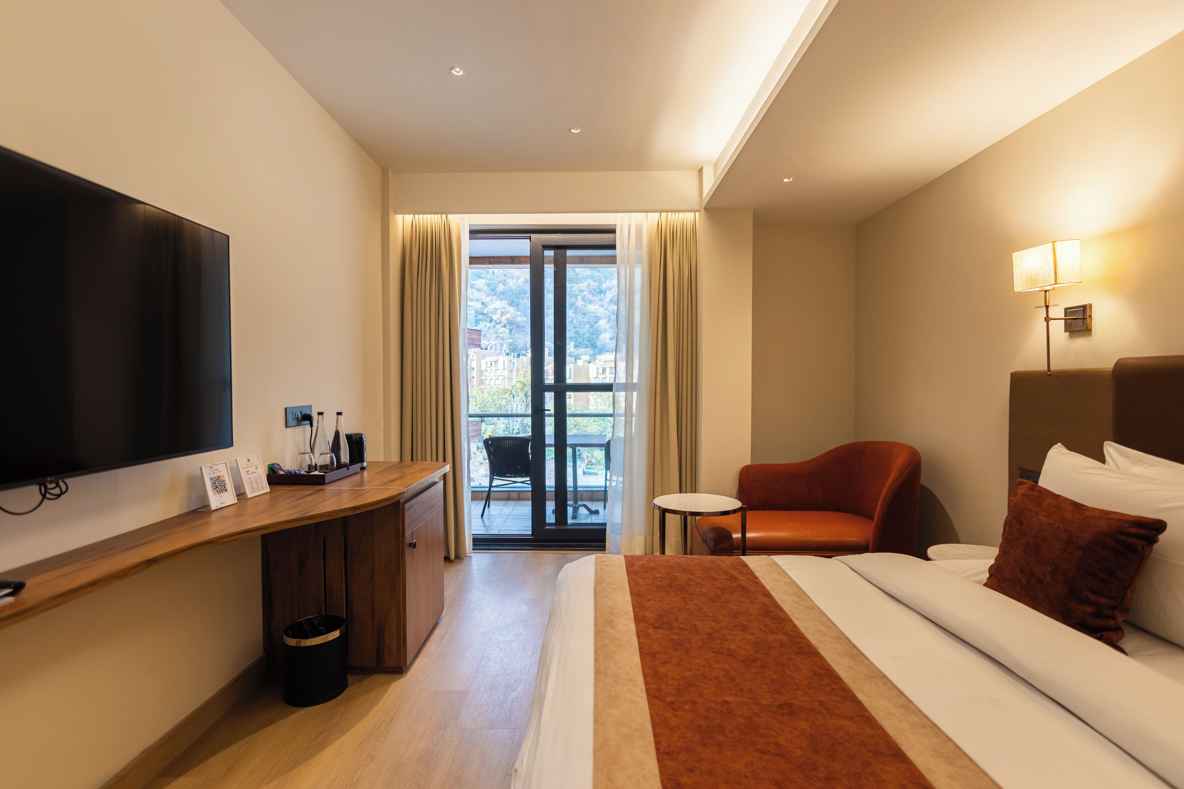 Habitación de hotel con cama, escritorio, televisión, silla y vistas al exterior.