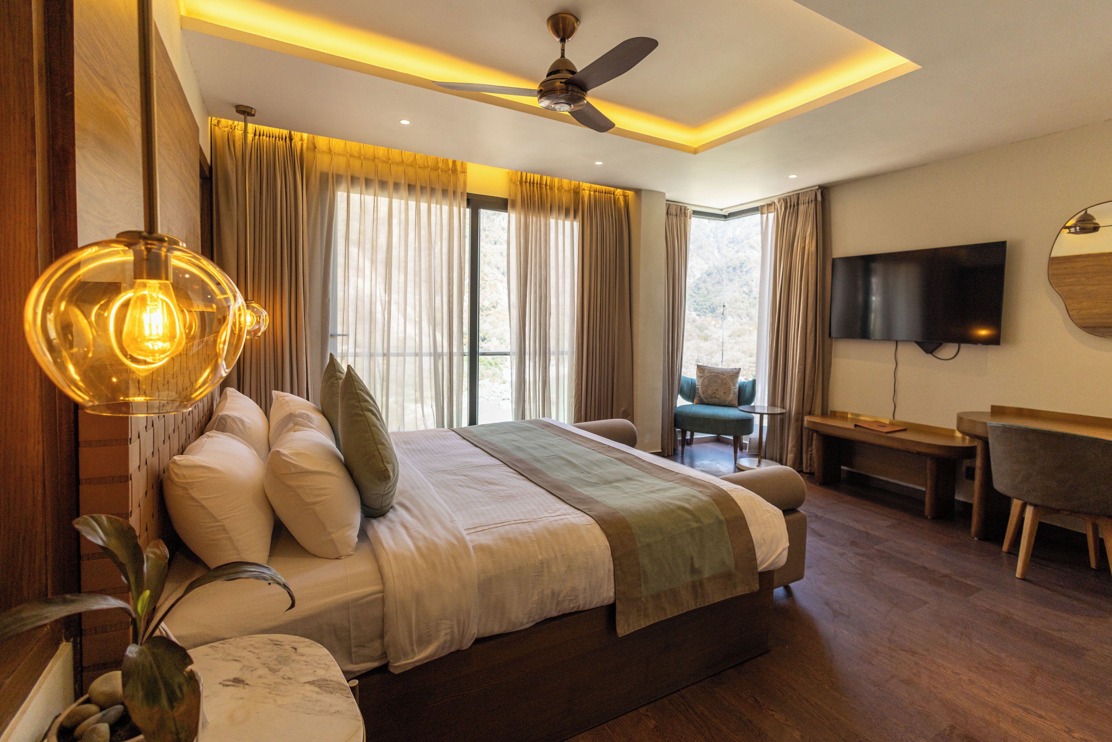 A modern hotel room with a large bed, a ceiling fan, a TV, and a view of the outdoors.