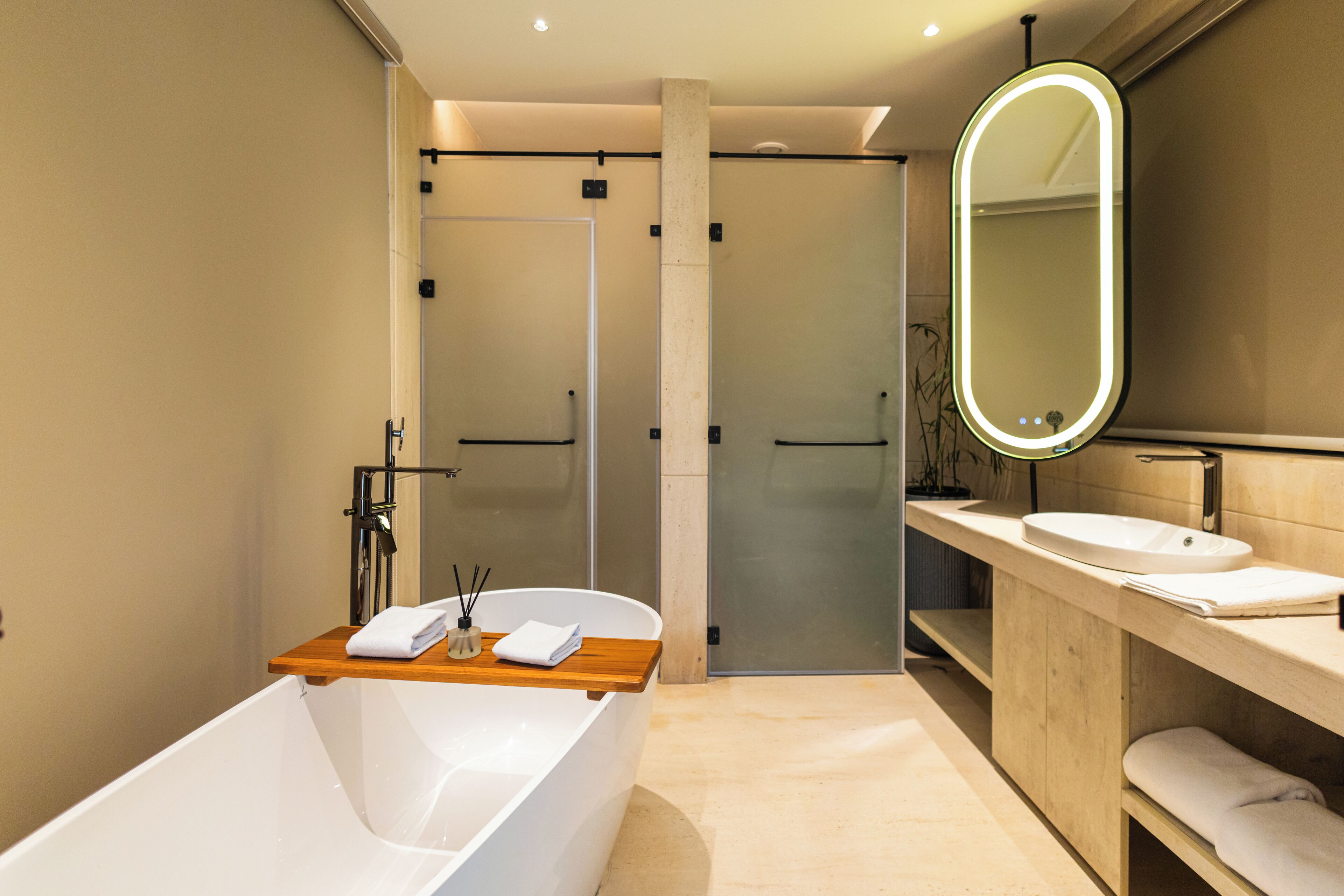 Un baño moderno con una bañera independiente, un tocador de madera y un espejo grande con marco iluminado.