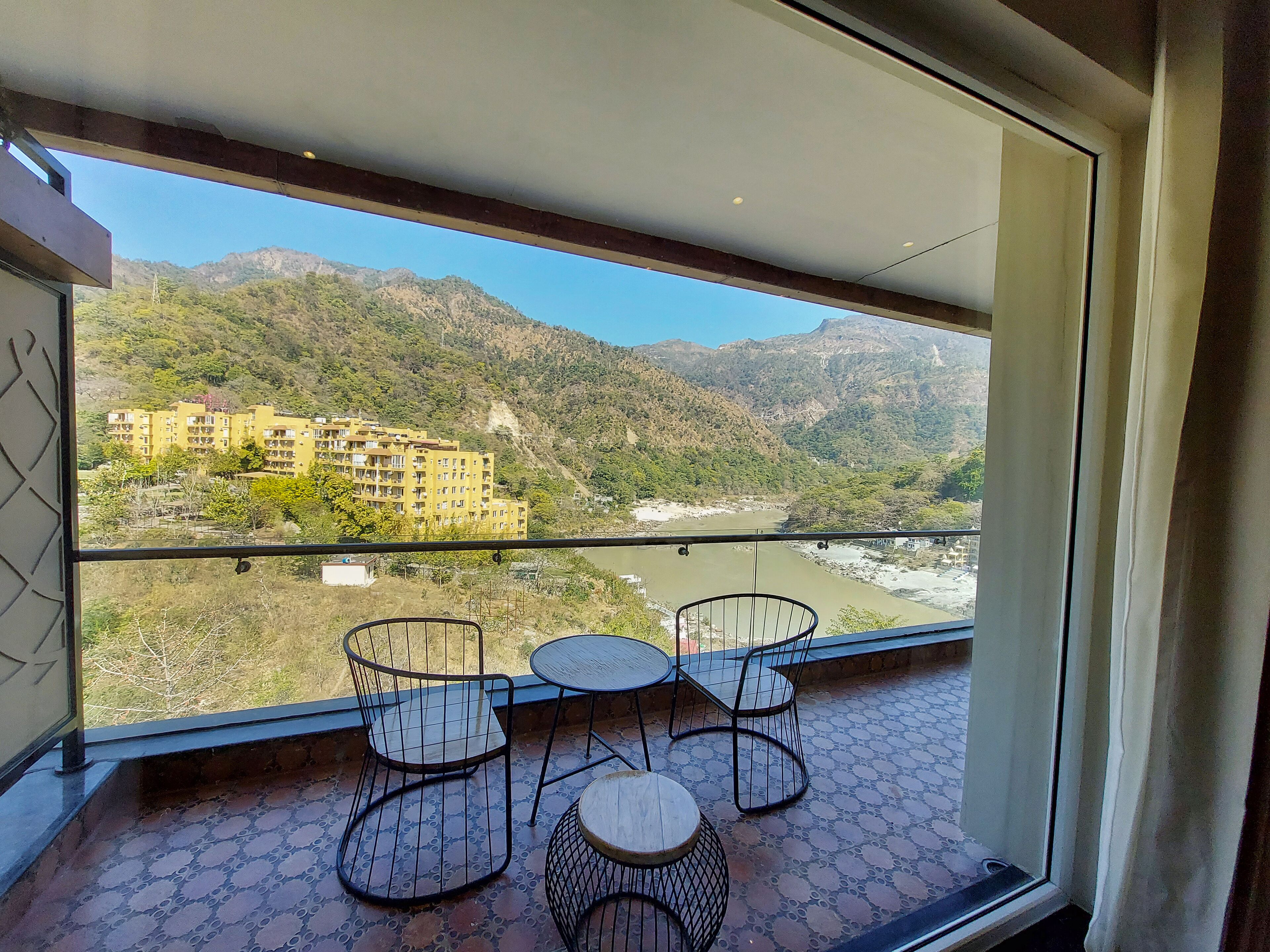 Een balkon met uitzicht op een rivier en bergen, met een tafel en stoelen.