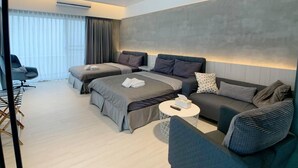 Una habitación de hotel moderna con una cama grande, dos camas más pequeñas, un sofá, una silla y una mesita redonda.
