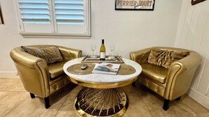 Ein Zimmer mit zwei goldenen Ledersofas, einem runden Tisch mit goldener Basis, einer Weinflasche und einem gerahmten Bild an der Wand.