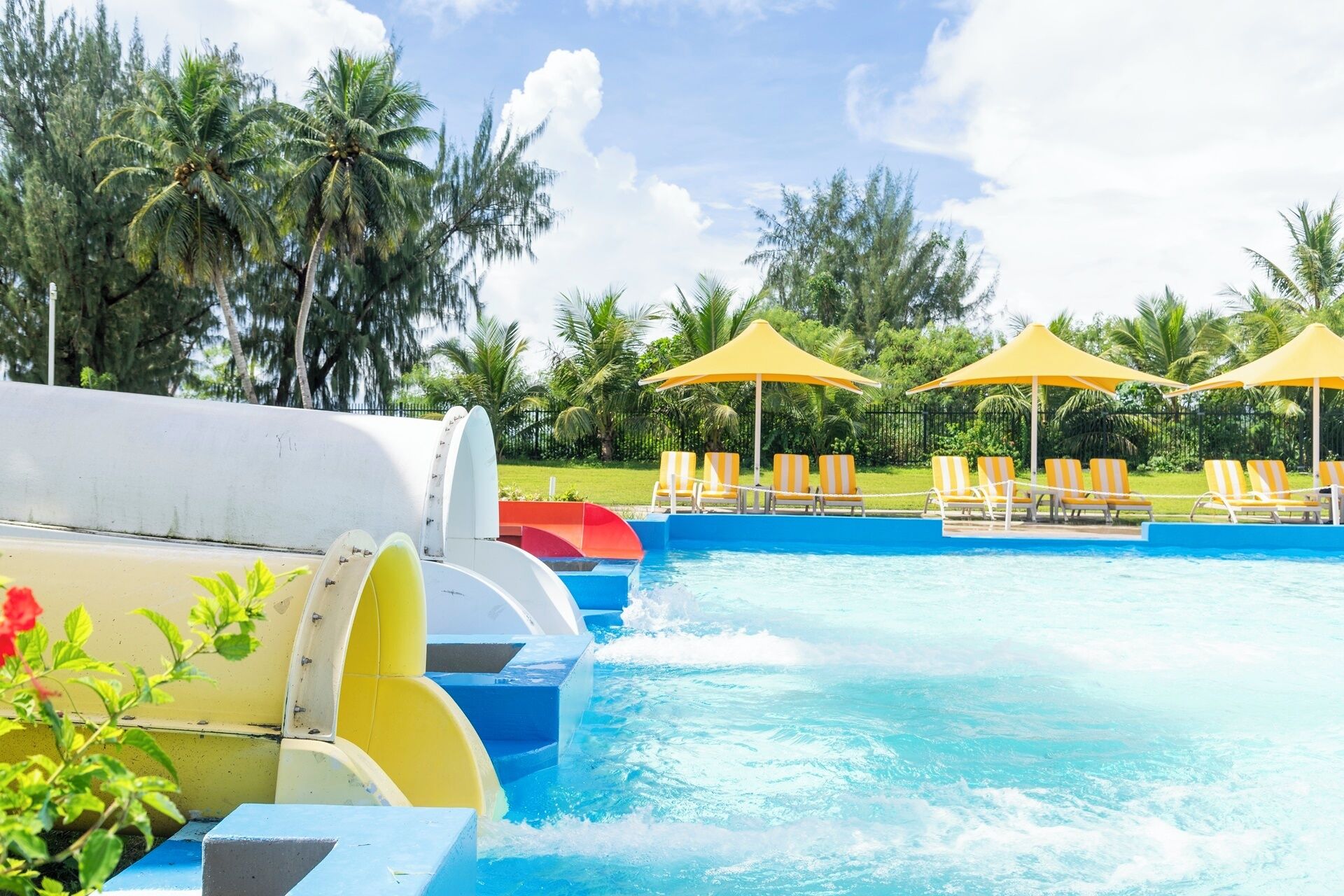 Un espace piscine doté de plusieurs toboggans, de chaises longues et de parasols.