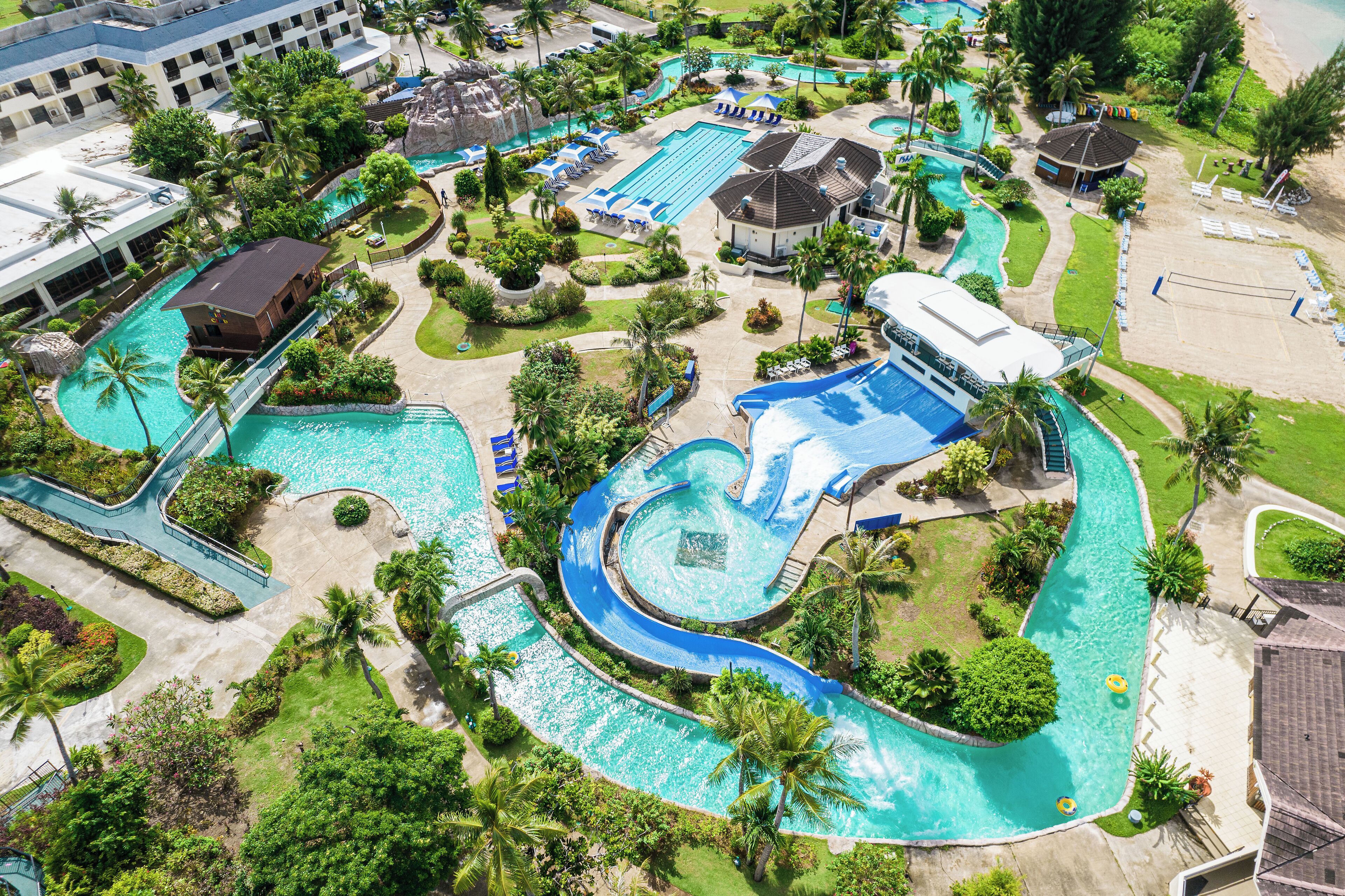 An aerial view of a resort with multiple swimming pools, palm trees, and a beach area.