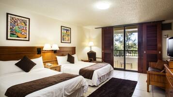 Quarto de hotel com duas camas, televisão, escrivaninha e varanda com vista para árvores.