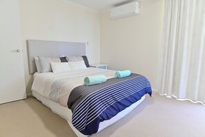 Een opgemaakt bed met strepen, een nachtkastje en een wandairconditioner.