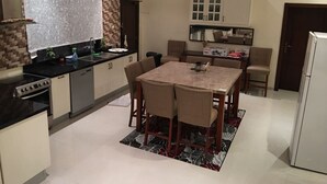 A modern kitchen with a dining area, featuring a central island, built-in appliances, and a large window with a decorative curtain. - Luxurious family  villa with fully furnished (Hidd)