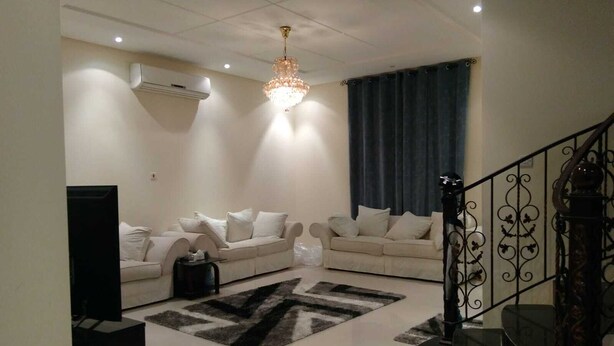 A living room with a sofa set, a chandelier, a staircase, and a black TV stand. - Luxurious family  villa with fully furnished (Hidd)