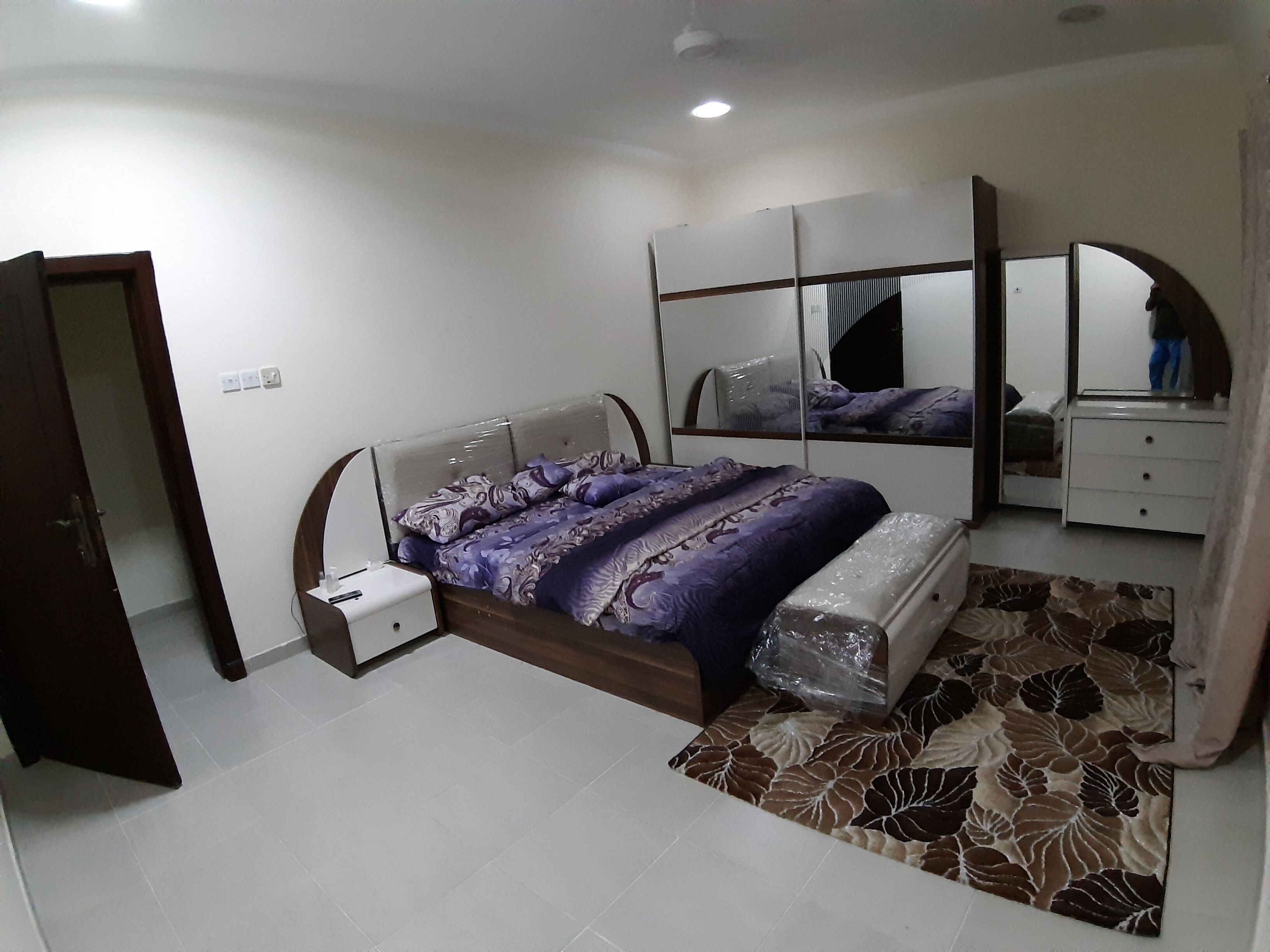 A bedroom with a bed, a nightstand, a dresser, a mirror, and a patterned rug.