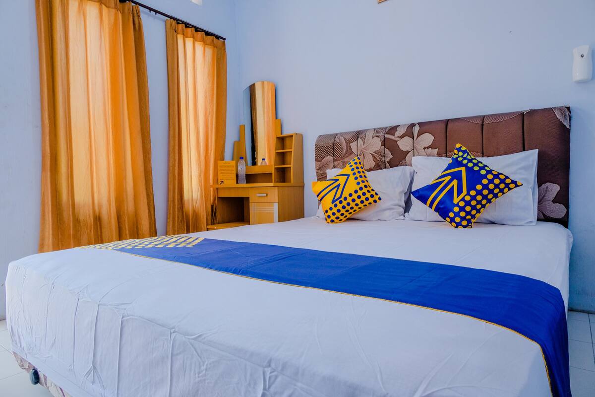 A neatly made bed with white and blue bedding, two pillows with blue and yellow patterns, and a wooden nightstand with a water bottle.