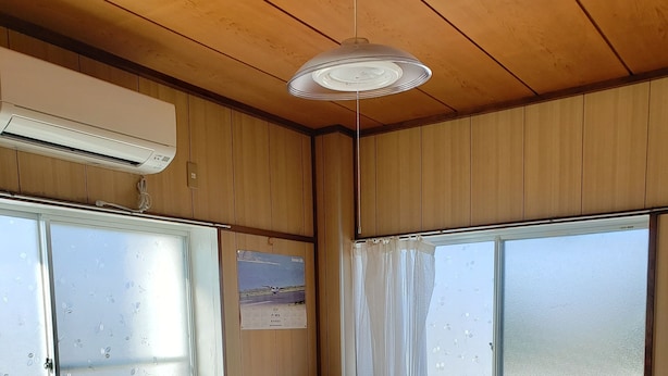 Een kamer met tatami vloerbedekking, een televisie op een standaard en een plafondventilator.